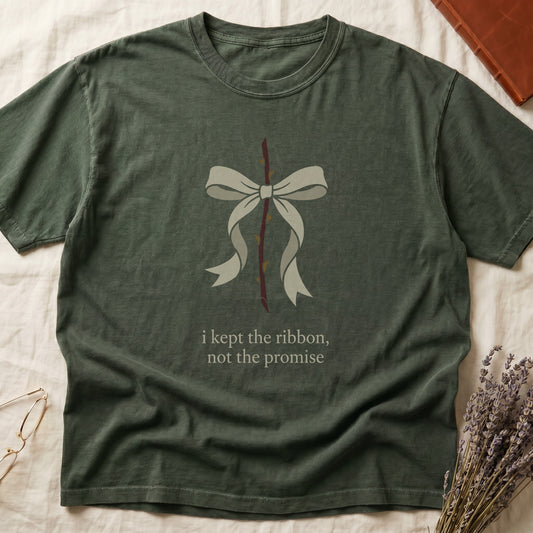 Green tee with cream bow tied around thorny rose stem, "i kept the ribbon, not the promise" in cream serif below.