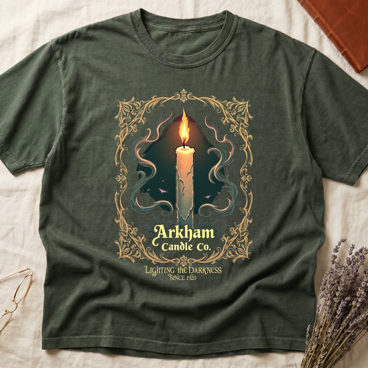 Green tee with lit candle, smoke, ornate gold filigree border, "Arkham Candle Co.," "Lighting the Darkness Since 1920."