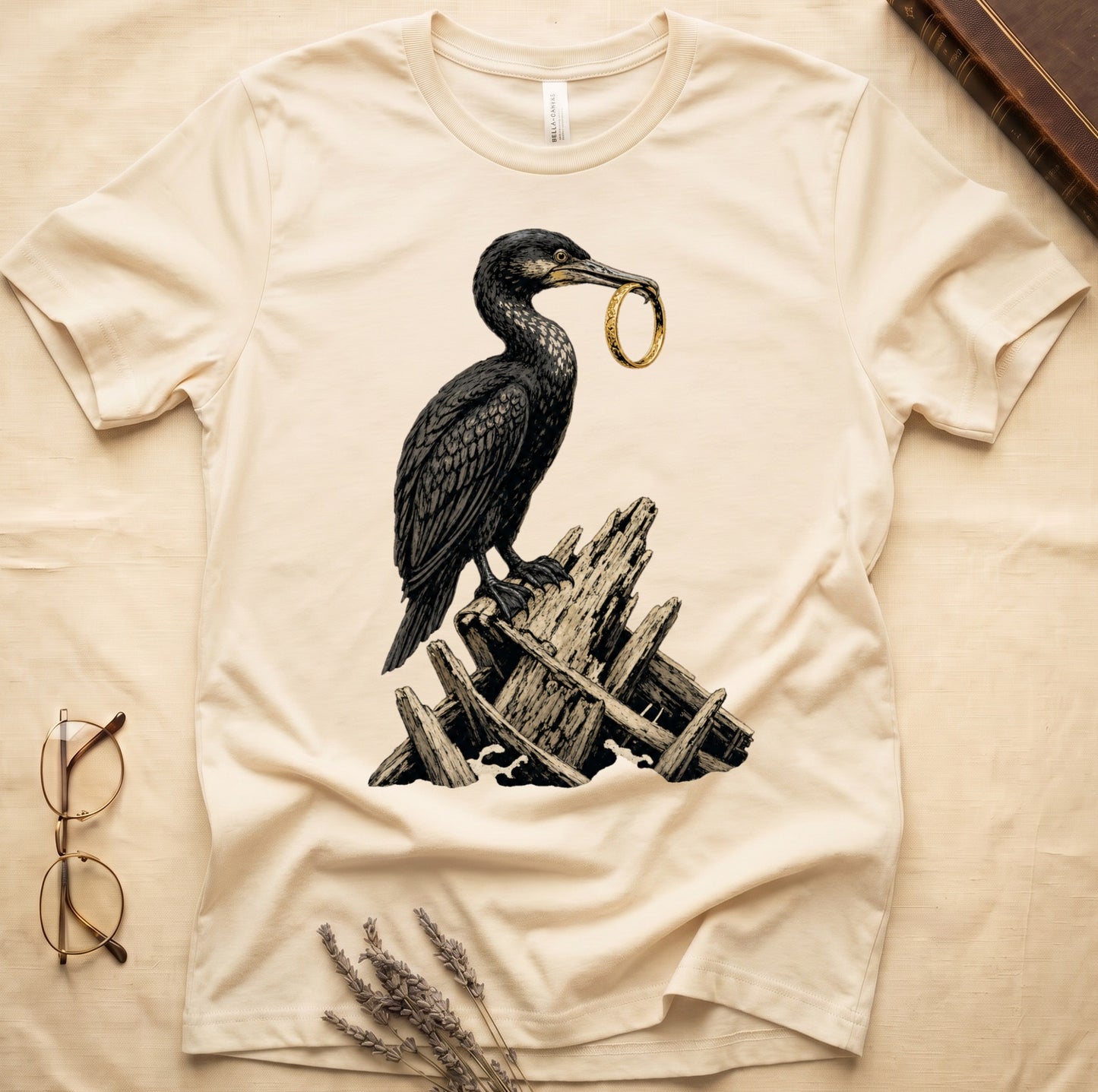 Cream t-shirt with black bird holding a gold ring over wooden wreckage.