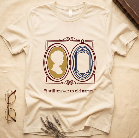 Natural tee with Victorian double-locket, silhouette portrait in gold frame, "i still answer to old names" cream serif below.