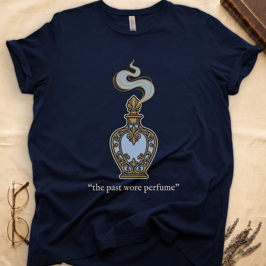 Navy tee with ornate blue and gold perfume bottle, rising scent swirl, "the past wore perfume" cream serif below.