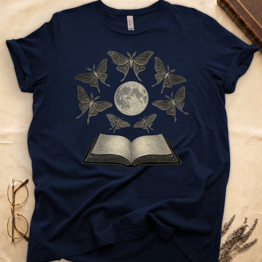 Navy tee with full moon center, seven luna moths in halo around, open book below, cream-on-black engraving.