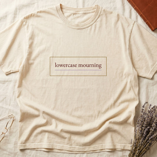 Ivory tee with "lowercase mourning" in cream serif inside gold rectangle frame, lavender line below.