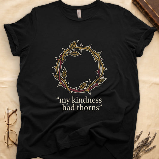 Black tee with crown of thorns in gold and red with green leaves, "my kindness had thorns" in cream serif.