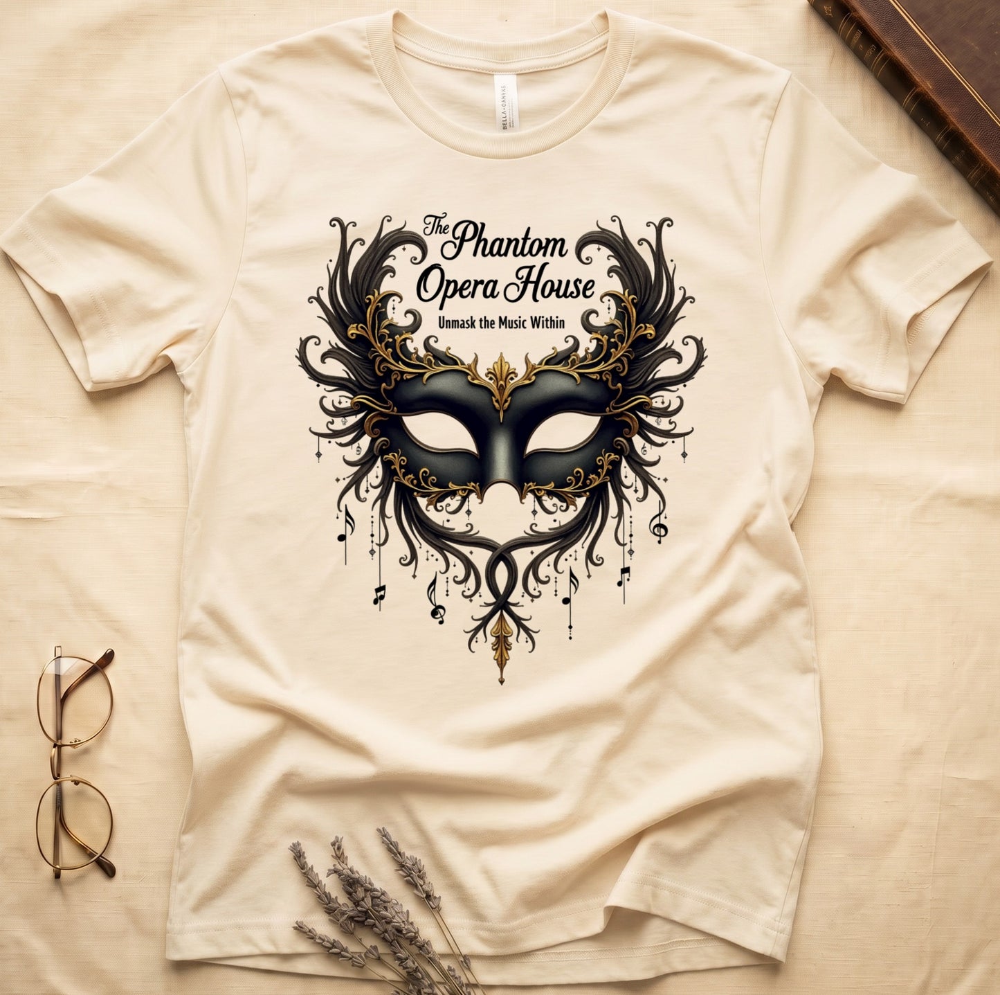 Natural tee with gold-and-black masquerade mask, scrollwork wings, "The Phantom Opera House," "Unmask the Music Within."