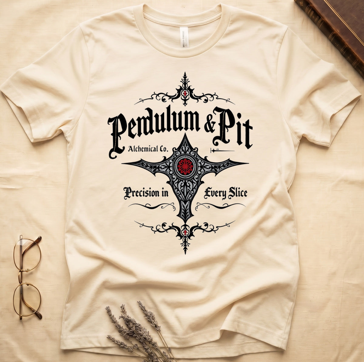 Natural tee with white talismanic cross, "Pendulum & Pit Alchemical Co.," "Precision in Every Slice" banner ribbons.