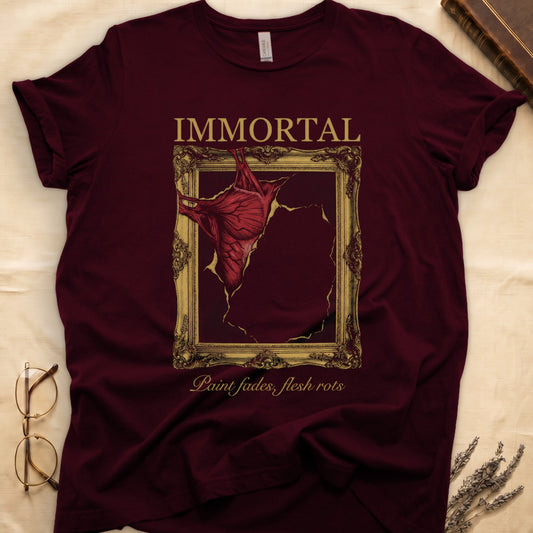 Maroon tee with gold frame and exposed muscle tearing canvas, "IMMORTAL" top, "Paint fades, flesh rots" italic below.