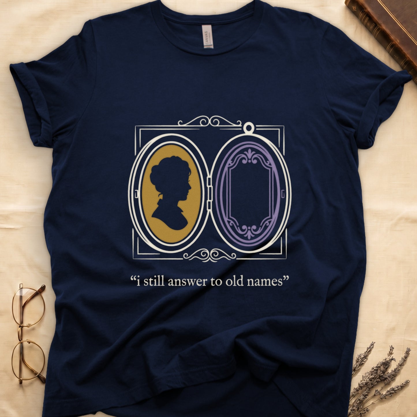 Navy tee with Victorian double-locket, silhouette portrait in gold frame, "i still answer to old names" cream serif below.