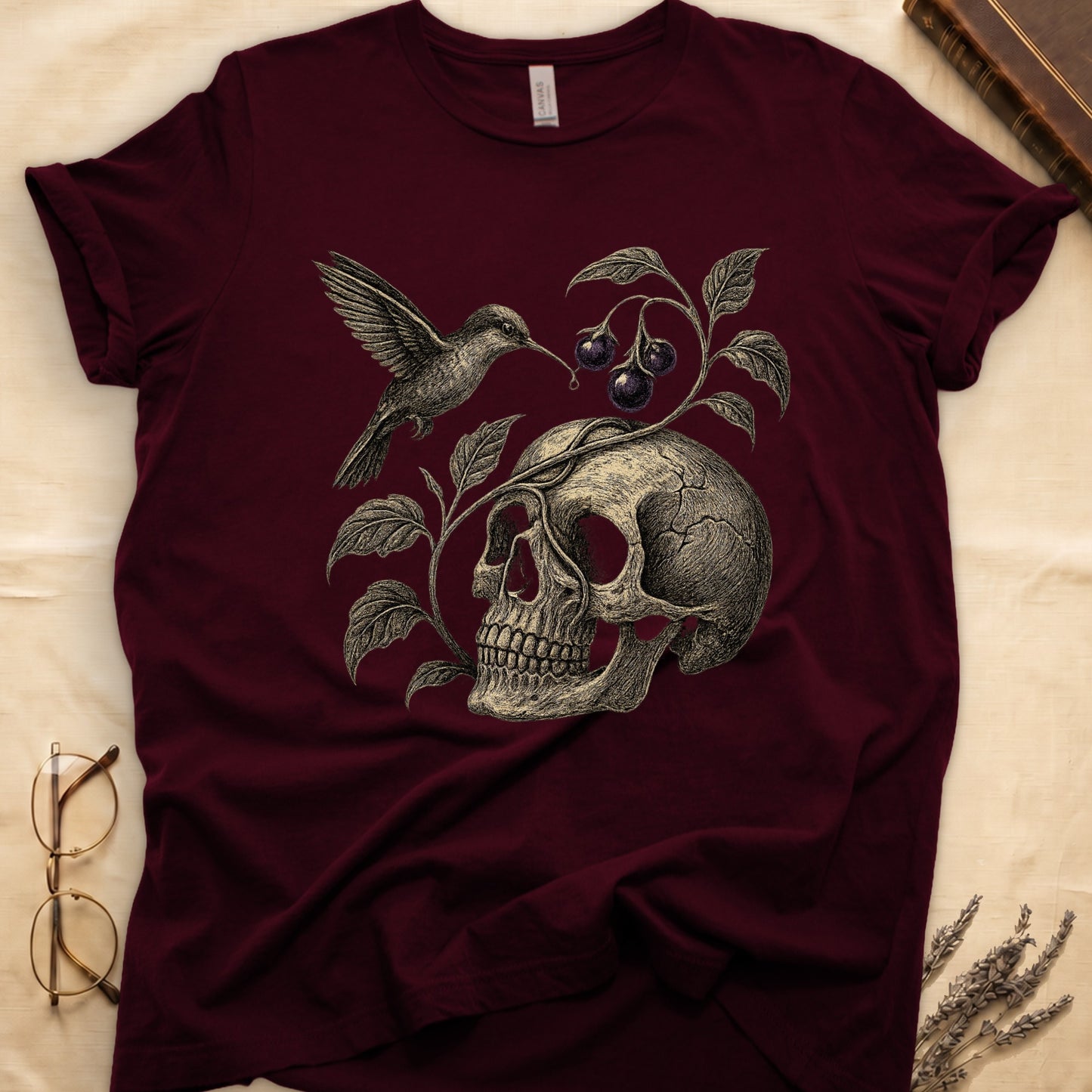 Maroon tee with sepia engraved skull, nightshade vine and dark-purple berries wrapping around, hummingbird at upper left.