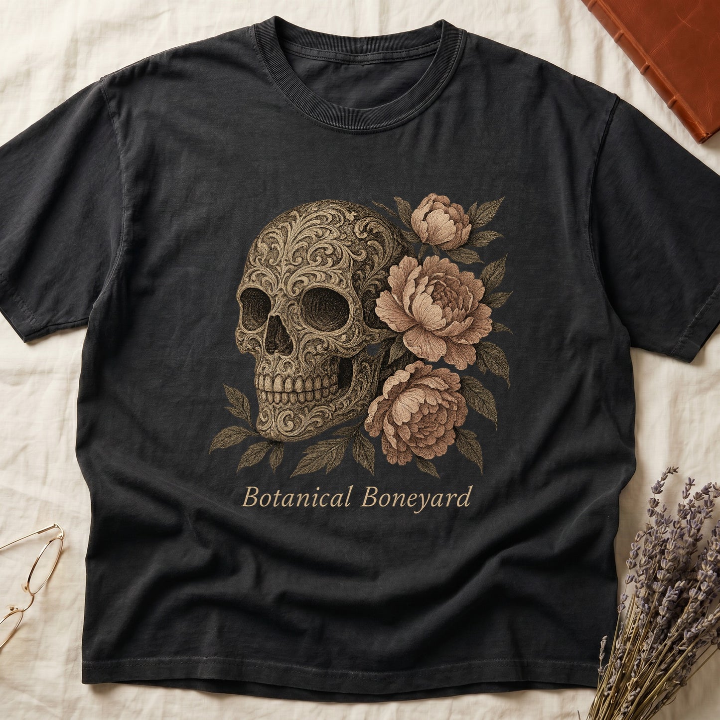 Black tee with filigree-engraved skull on left, peach-cream peonies on right, crossed bones below, "Botanical Boneyard."