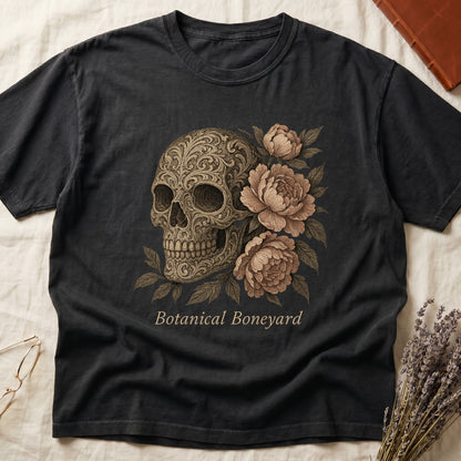 Black tee with filigree-engraved skull on left, peach-cream peonies on right, crossed bones below, "Botanical Boneyard."