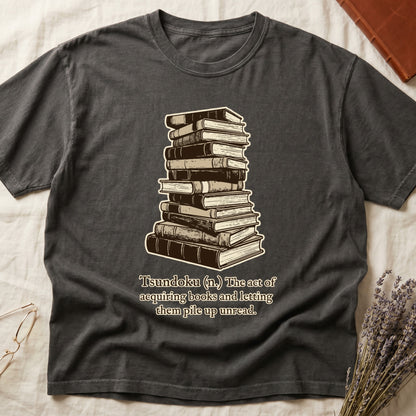 Pepper tee with stack of vintage hardcovers, "Tsundoku (n.) The act of acquiring books and letting them pile up unread."