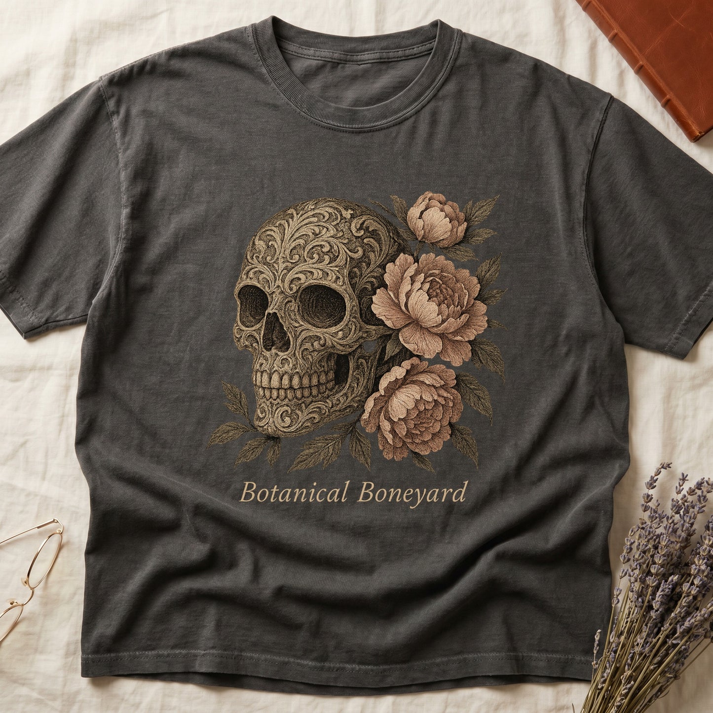 Pepper tee with filigree-engraved skull on left, peach-cream peonies on right, crossed bones below, "Botanical Boneyard."