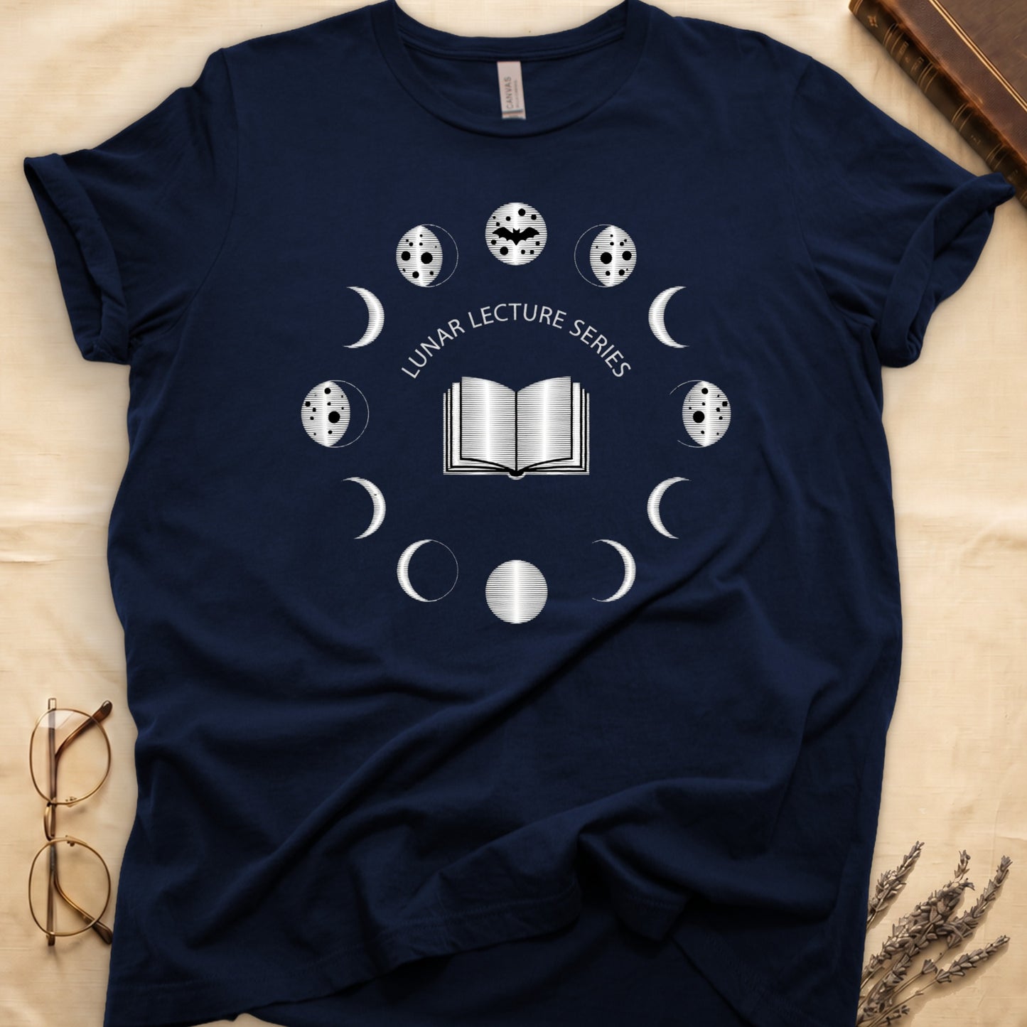 Navy tee with open book at center, ring of cream moon phases around, curved "LUNAR LECTURE SERIES" double-arc above.