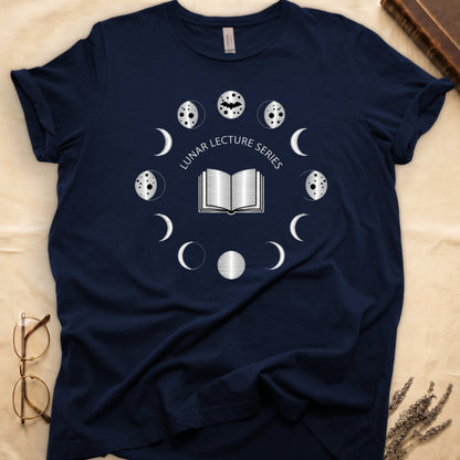 Navy tee with open book at center, ring of cream moon phases around, curved "LUNAR LECTURE SERIES" double-arc above.