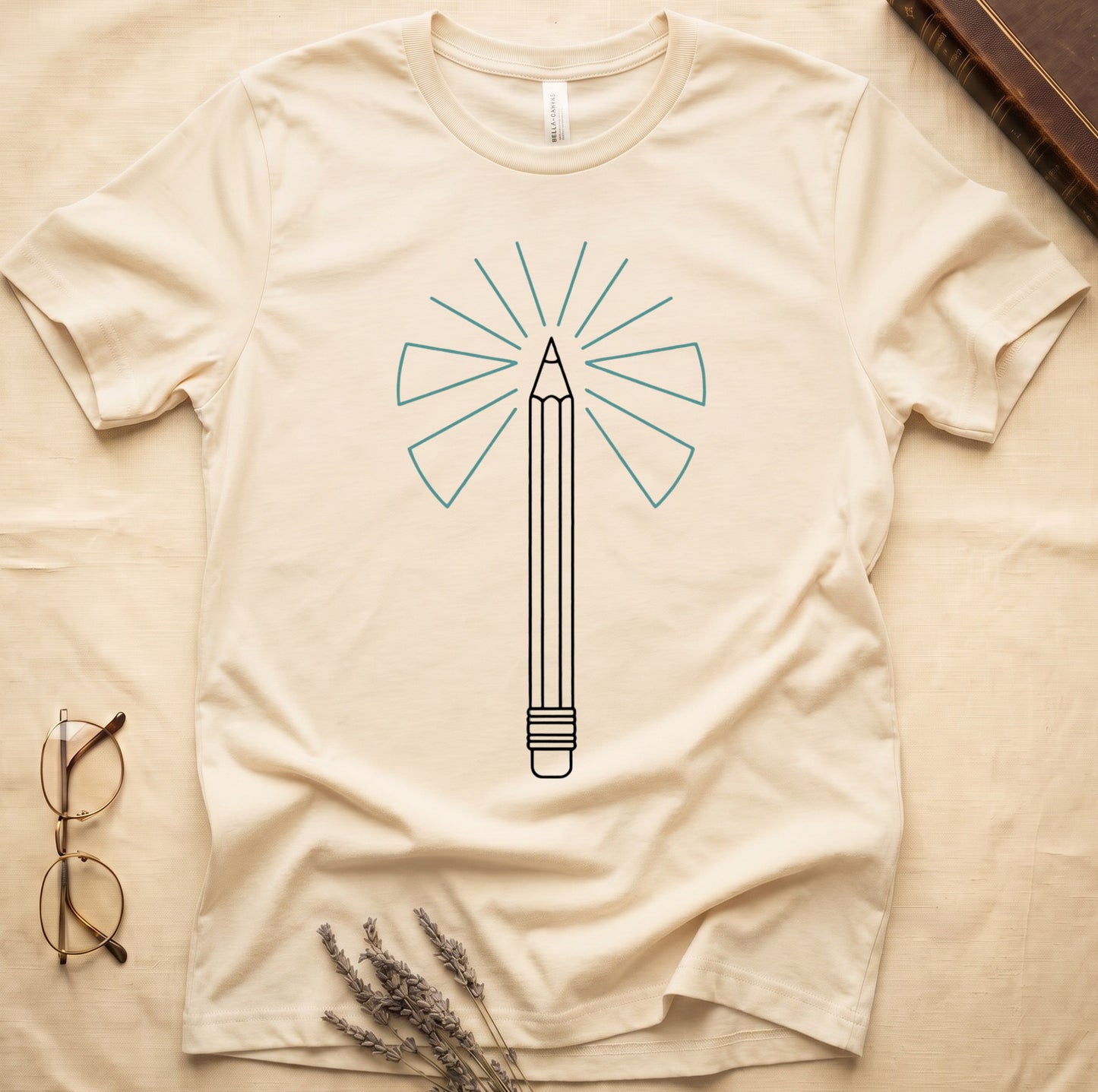 Natural tee with single vertical graphite pencil in cream linework, fan of teal and grey rays radiating behind.