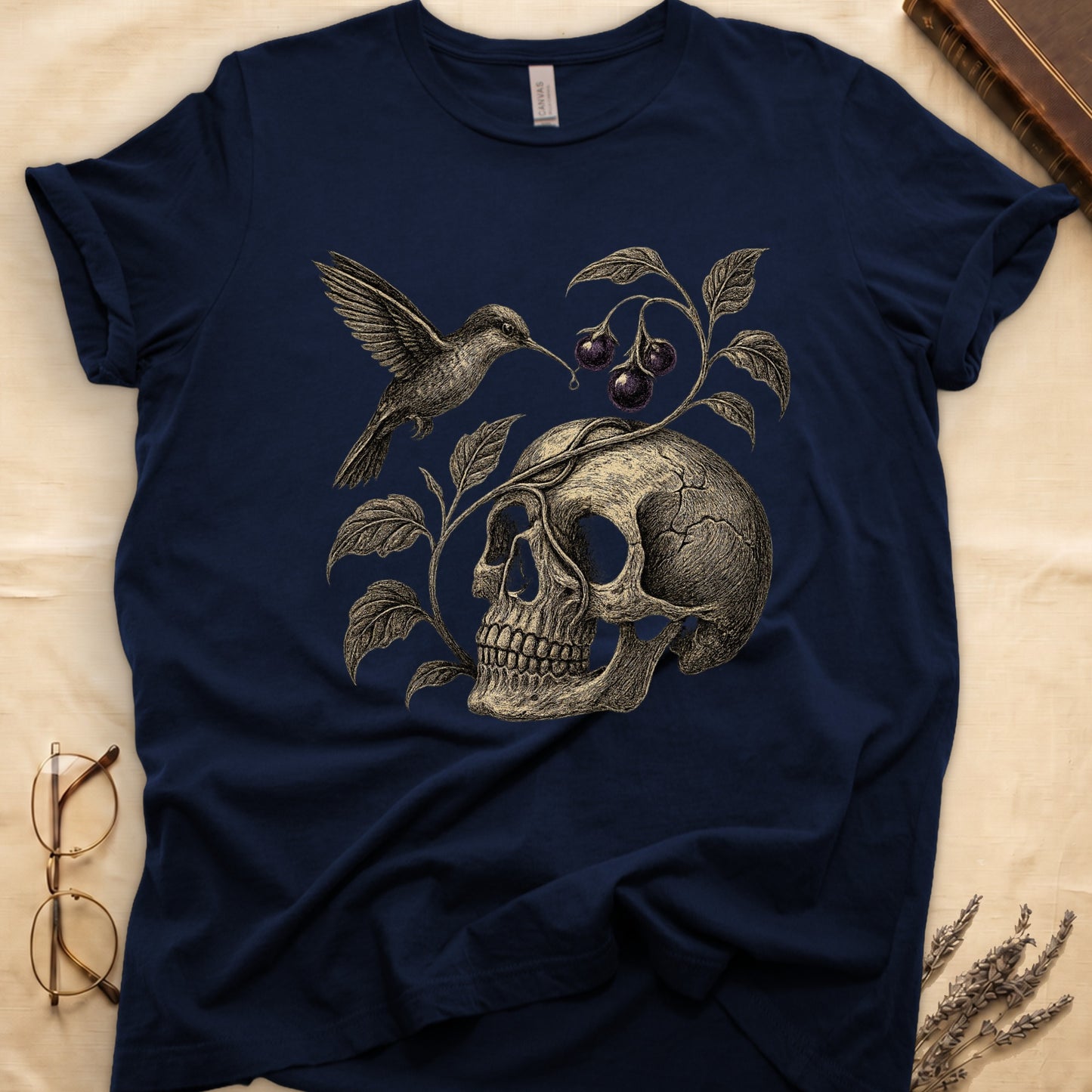 Navy tee with sepia engraved skull, nightshade vine and dark-purple berries wrapping around, hummingbird at upper left.