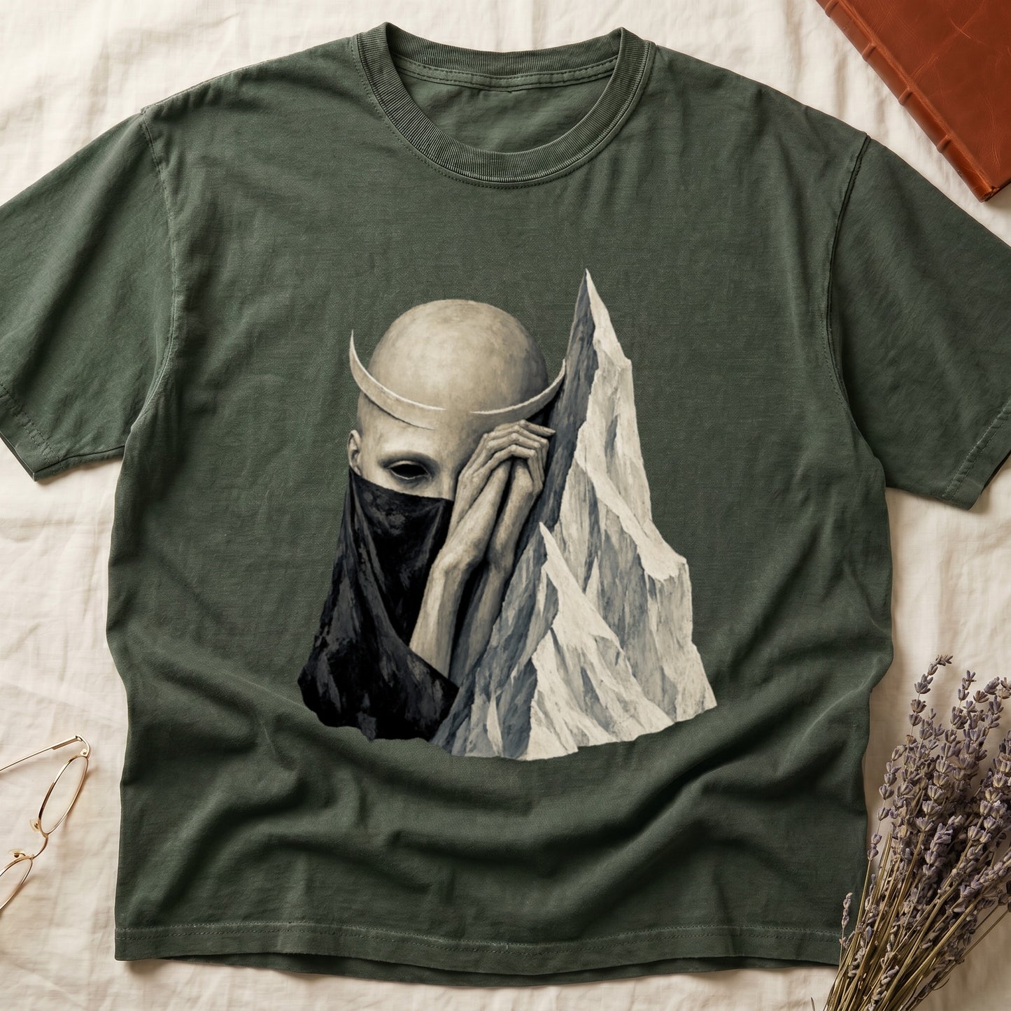 Green t-shirt with graphic of a bald figure with horns, dark veil, and mountain.
