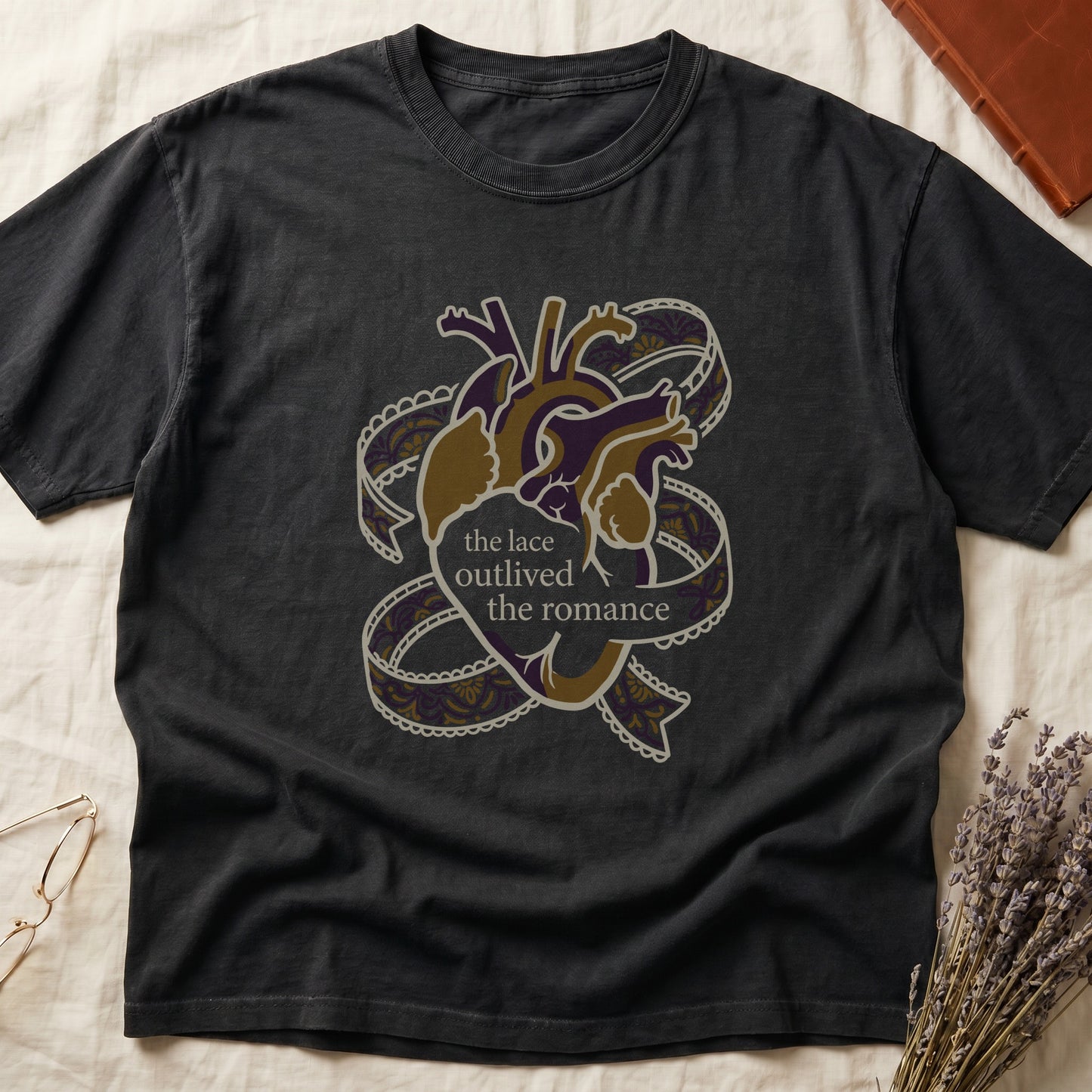 Black tee with anatomical heart in purple and gold wrapped in lace ribbons, "the lace outlived the romance" in serif.