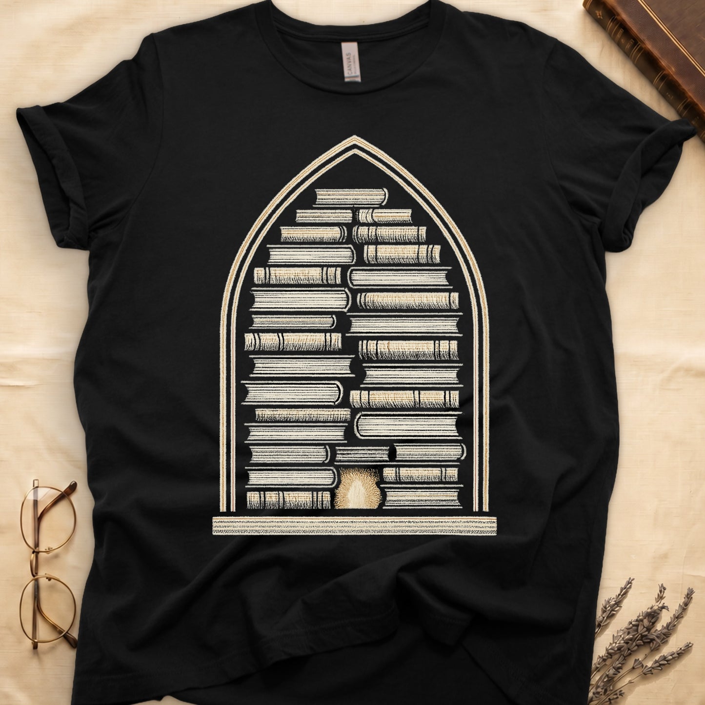 Black tee with gothic arch frame, columns of leather-bound books inside, sunburst medallion at base, cream engraved linework.