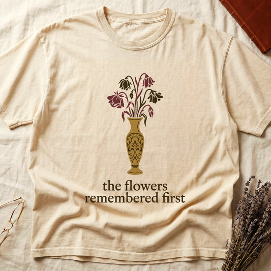 Ivory tee with gold ornate vase, wilting cream lilies and dark red roses, "the flowers remembered first" in cream serif.