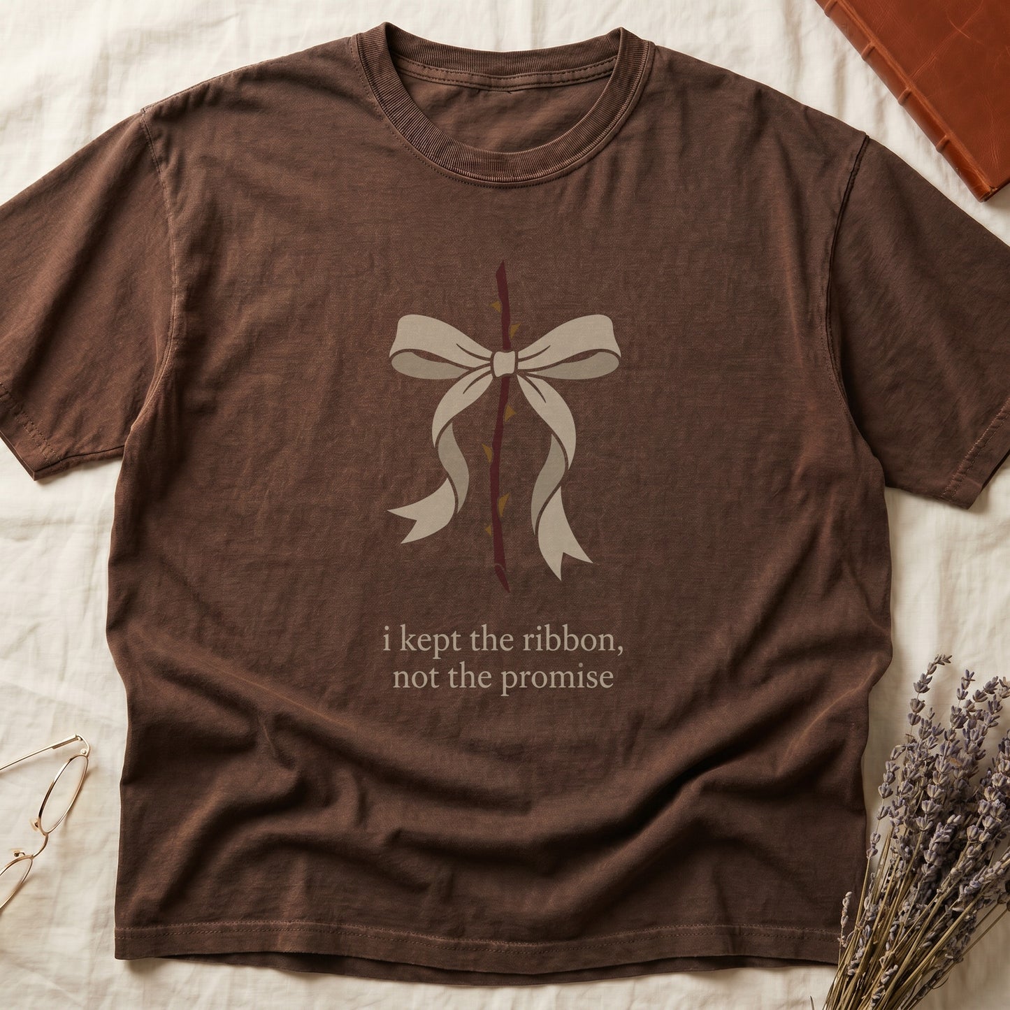 Espresso tee with cream bow tied around thorny rose stem, "i kept the ribbon, not the promise" in cream serif below.