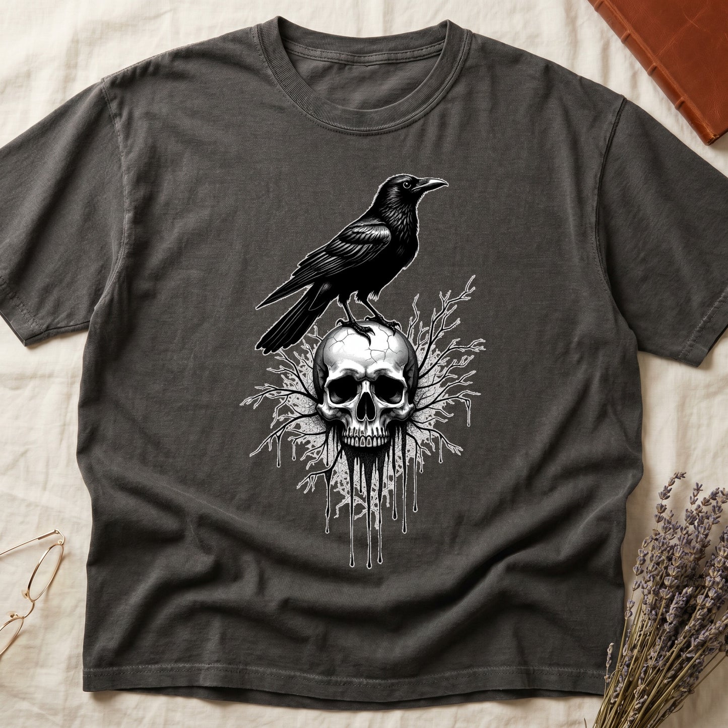 Pepper tee with raven silhouette on human skull, ink drips from jaw, bare branches behind, monochrome illustration.