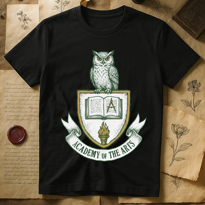 Black tee with heraldic shield crest, owl perched on top, open book and dividers center, "ACADEMY OF THE ARTS" on a banner.