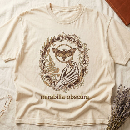 Ivory tee with skeletal hand, magnifying glass, death's-head moth, ferns on green, "mīrābilia obscūra" in Latin italic.
