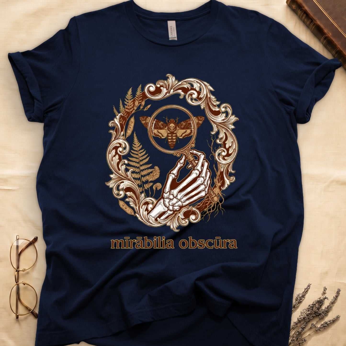 Navy tee with skeletal hand, magnifying glass, death's-head moth, ferns on green, "mīrābilia obscūra" in Latin italic.