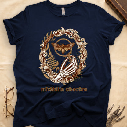 Navy tee with skeletal hand, magnifying glass, death's-head moth, ferns on green, "mīrābilia obscūra" in Latin italic.