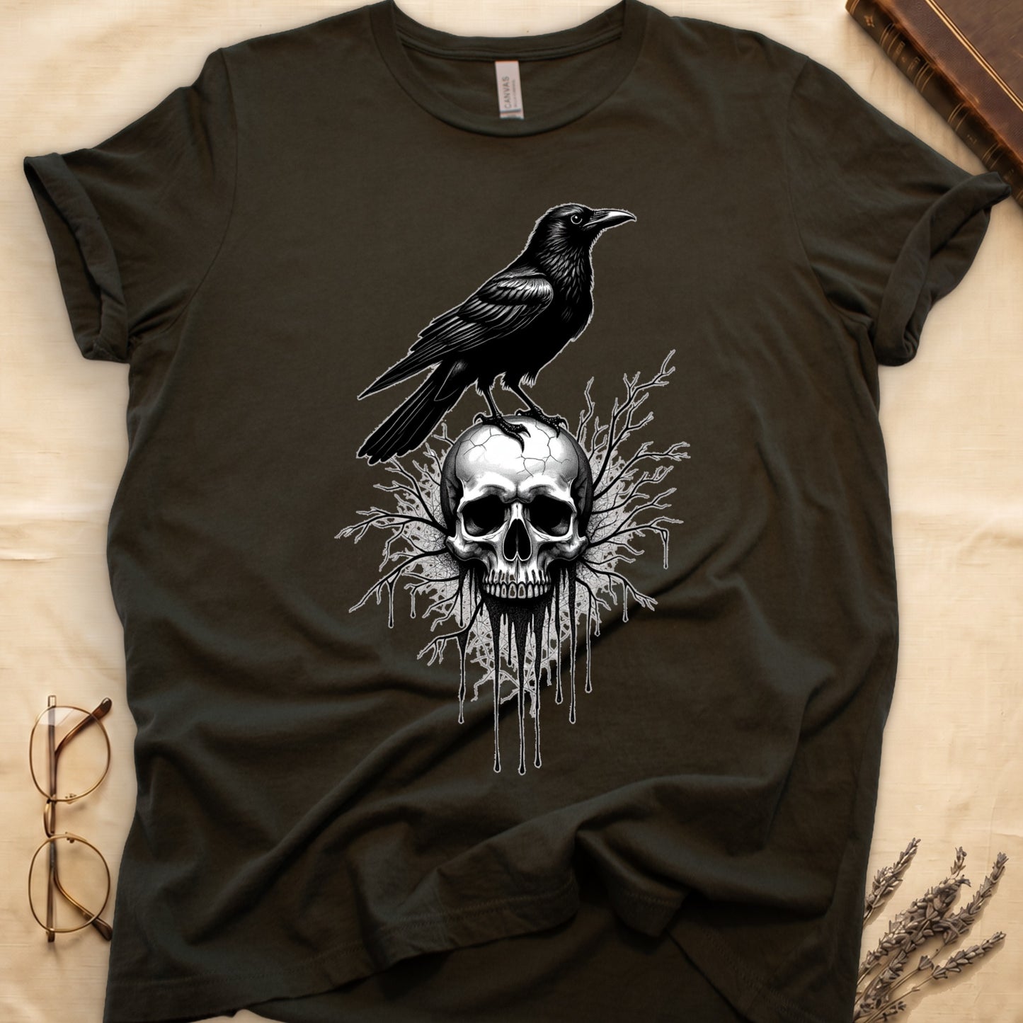 Military Green tee with raven silhouette on human skull, ink drips from jaw, bare branches behind, monochrome illustration.