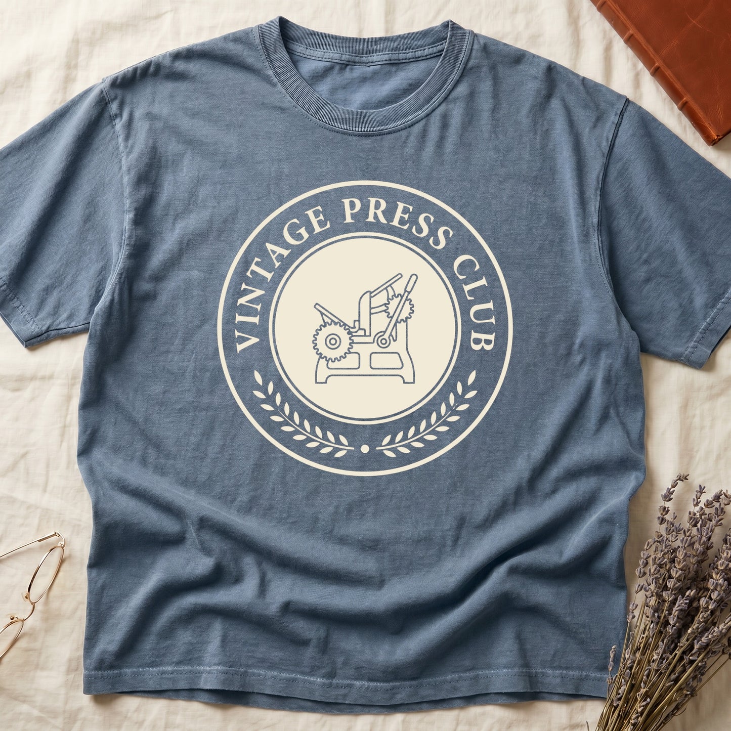 Blue Jean tee with circular letterpress badge, "VINTAGE PRESS CLUB" in serif capitals, antique printing press in cream linework.