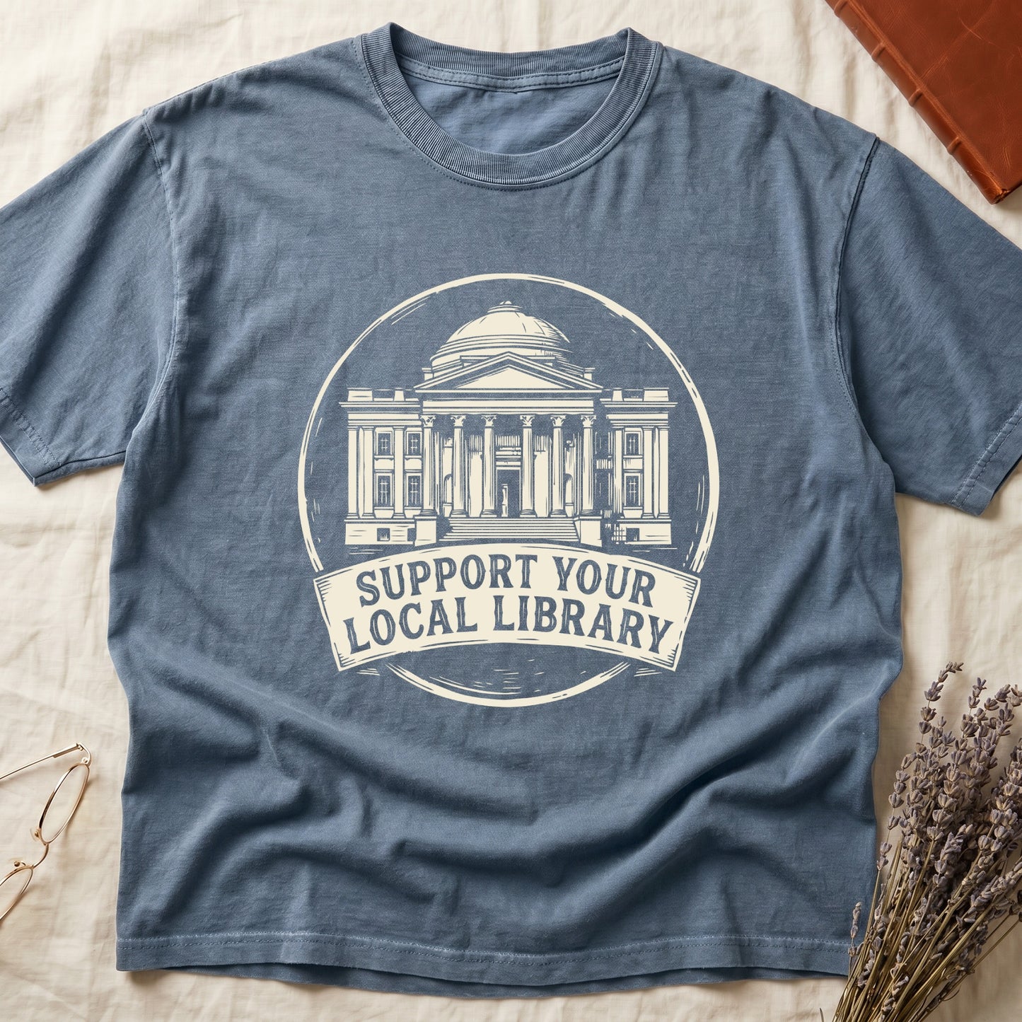 Blue Jean tee with circular cream badge of a classical library building, "SUPPORT YOUR LOCAL LIBRARY" on a banner below.