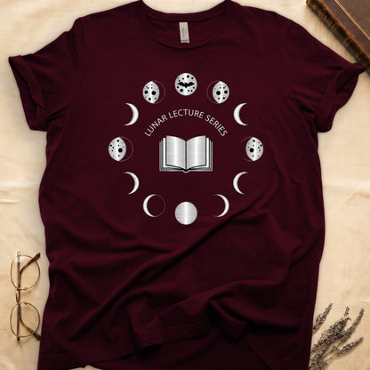 Maroon tee with open book at center, ring of cream moon phases around, curved "LUNAR LECTURE SERIES" double-arc above.
