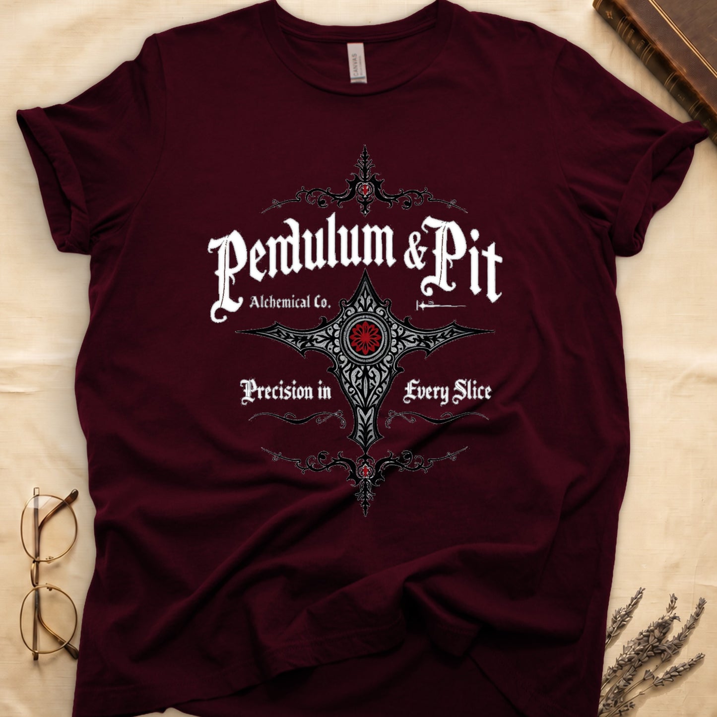 Maroon tee with white talismanic cross, "Pendulum & Pit Alchemical Co.," "Precision in Every Slice" banner ribbons.