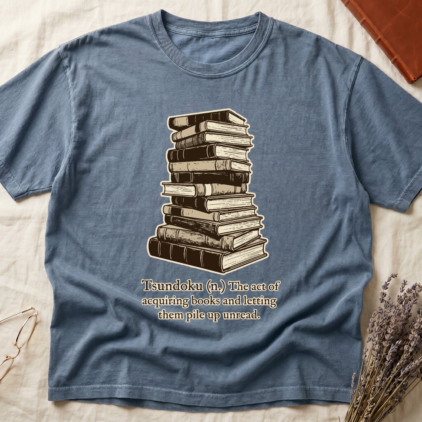 Blue Jean tee with stack of vintage hardcovers, "Tsundoku (n.) The act of acquiring books and letting them pile up unread."