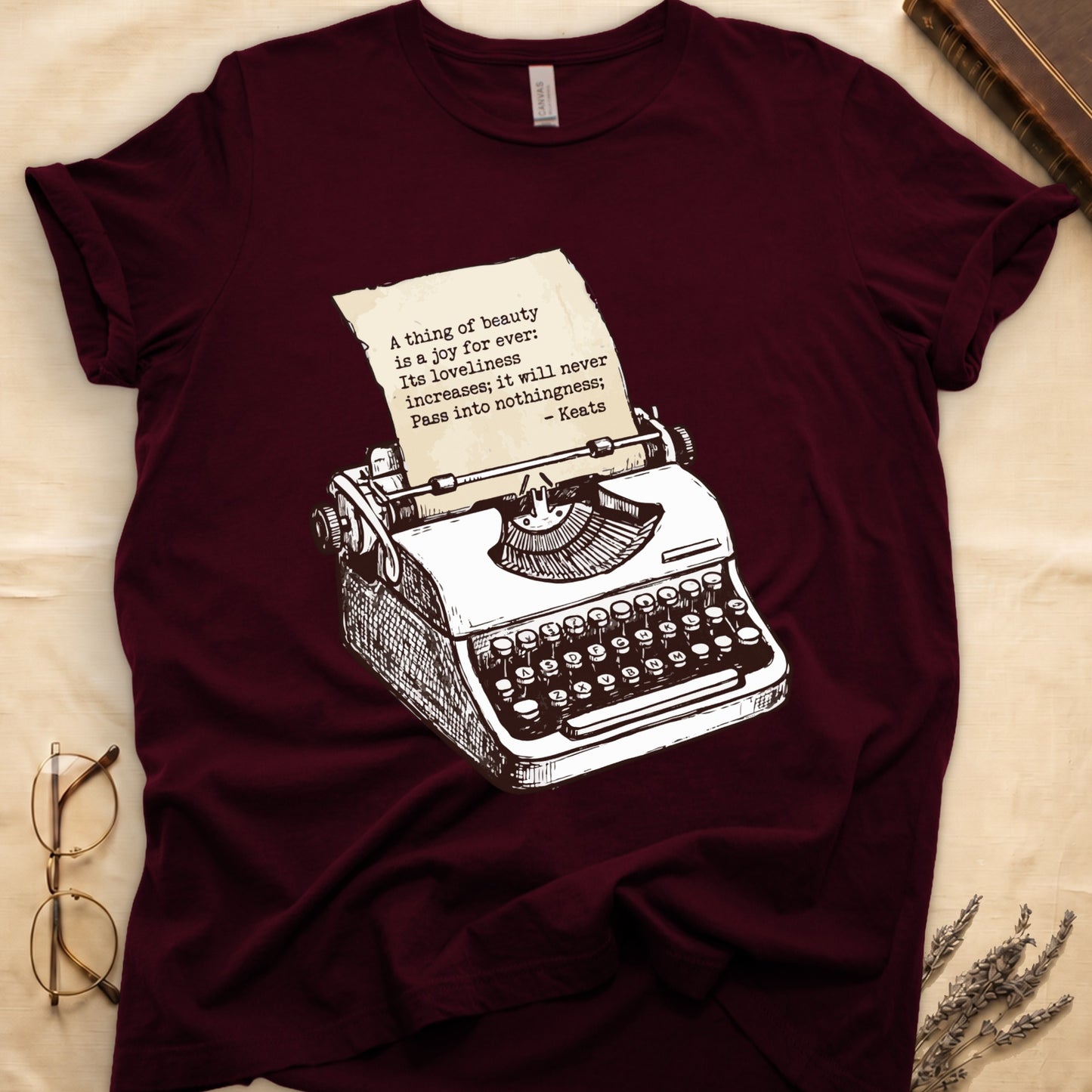 Maroon tee with vintage typewriter in cream linework, paper showing "A thing of beauty is a joy for ever" by Keats.