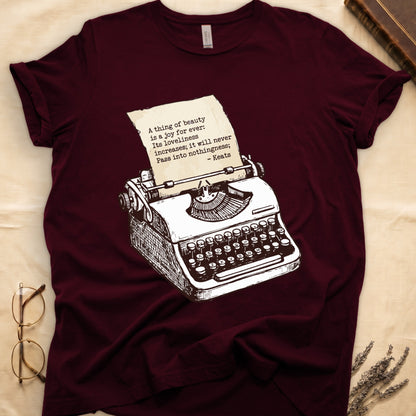 Maroon tee with vintage typewriter in cream linework, paper showing "A thing of beauty is a joy for ever" by Keats.