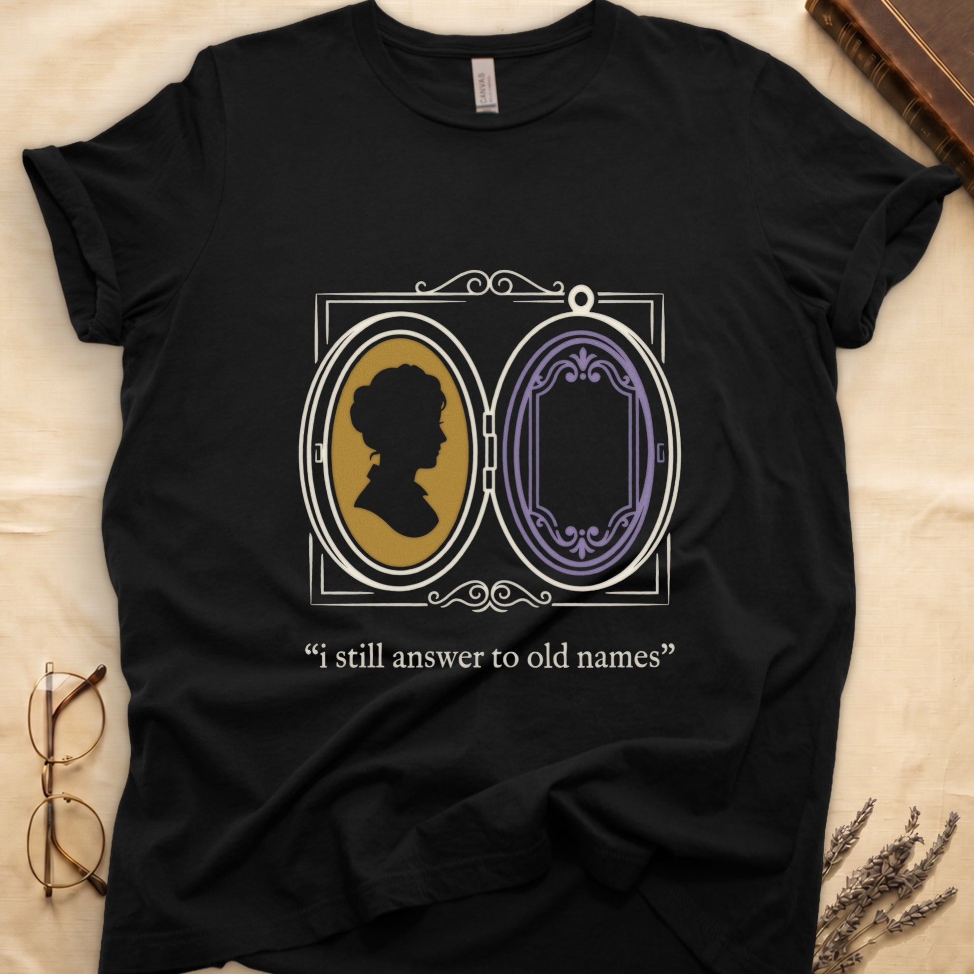Black tee with Victorian double-locket, silhouette portrait in gold frame, "i still answer to old names" cream serif below.
