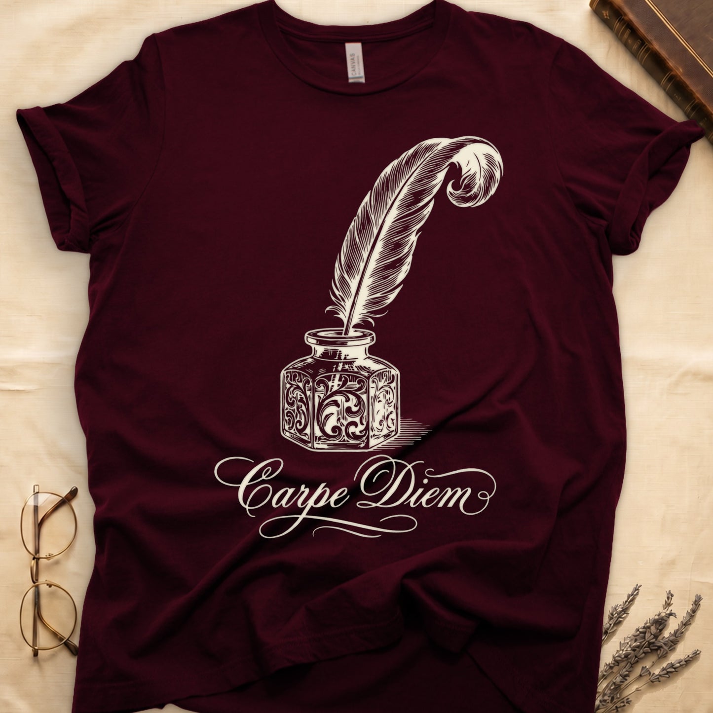 Maroon tee with ornate antique inkwell and quill pen in sepia linework, "Carpe Diem" in flowing cursive below.