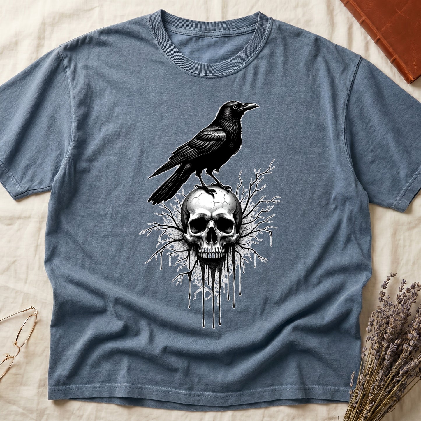 Blue Jean tee with raven silhouette on human skull, ink drips from jaw, bare branches behind, monochrome illustration.