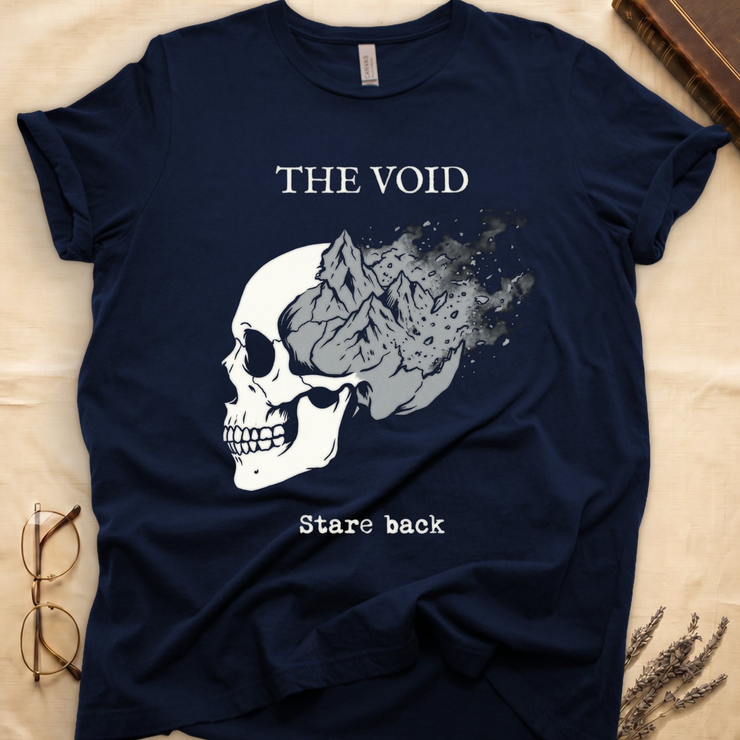 Navy tee with skull eroding into mountain landscape and stardust, "THE VOID" top, "Stare back" typewriter below.
