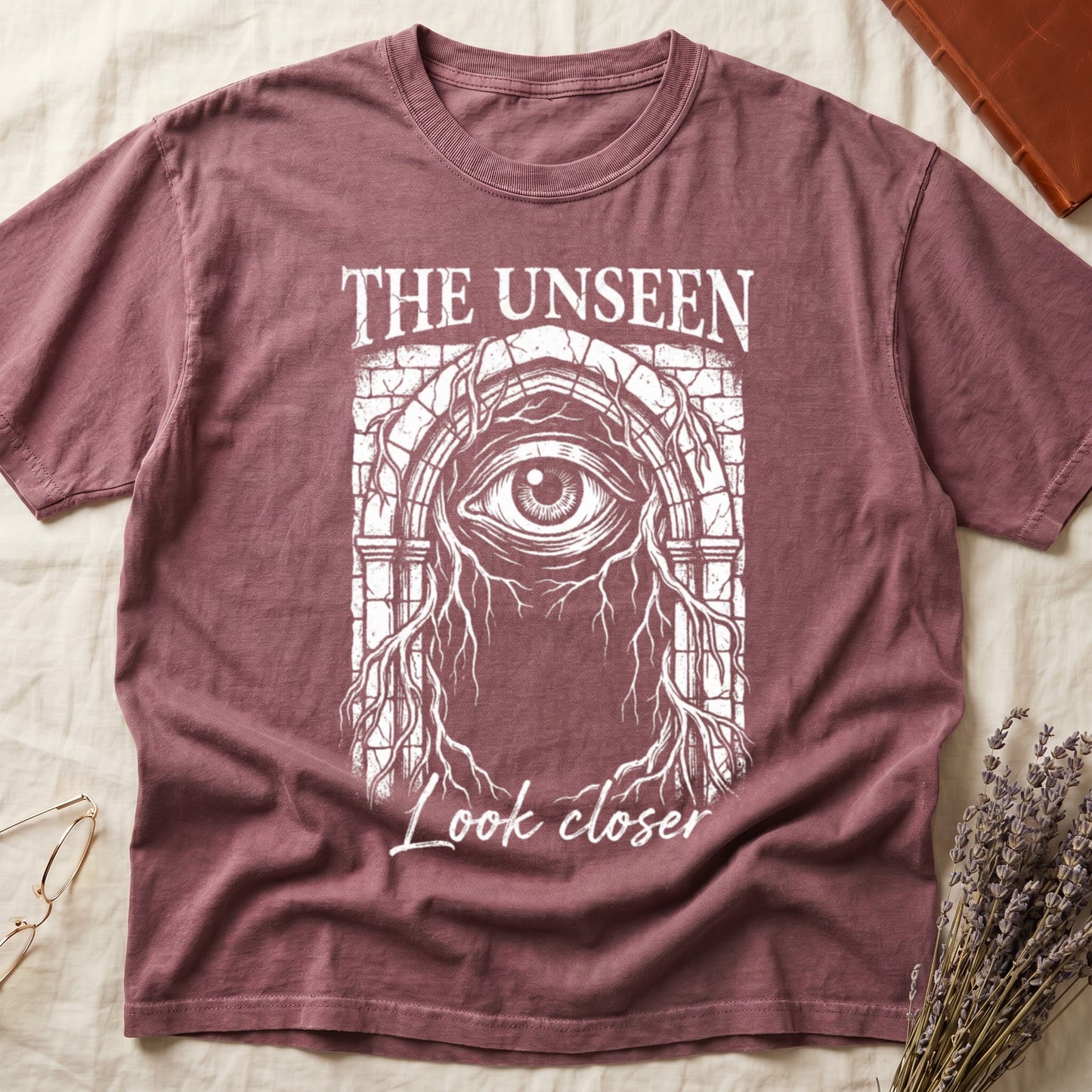 Dark Rose tee with Gothic stone arch, open eye, roots trailing, "THE UNSEEN" top, "Look closer" cursive below.