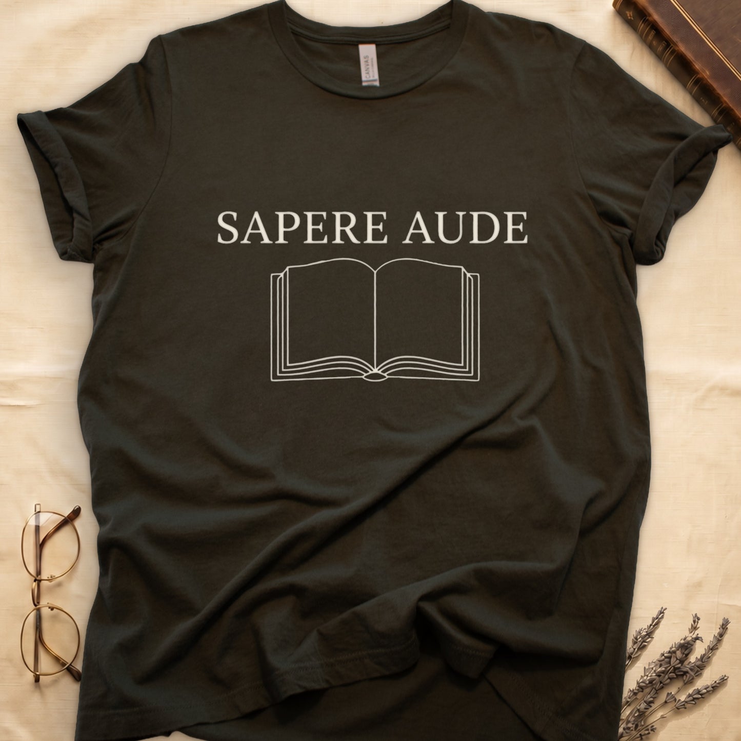 Military Green tee with "SAPERE AUDE" in serif capitals above a minimalist open book in cream linework.