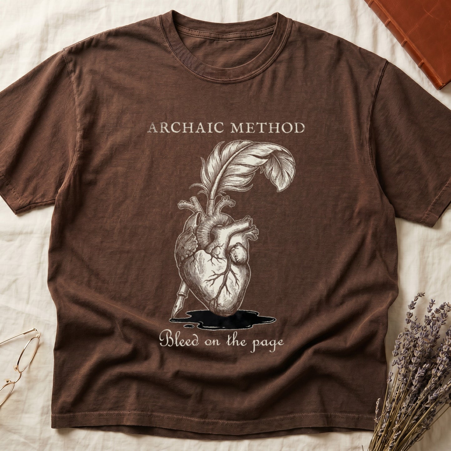 Espresso tee with anatomical heart and quill emerging in cream linework, "ARCHAIC METHOD" top, "Bleed on the page" below.