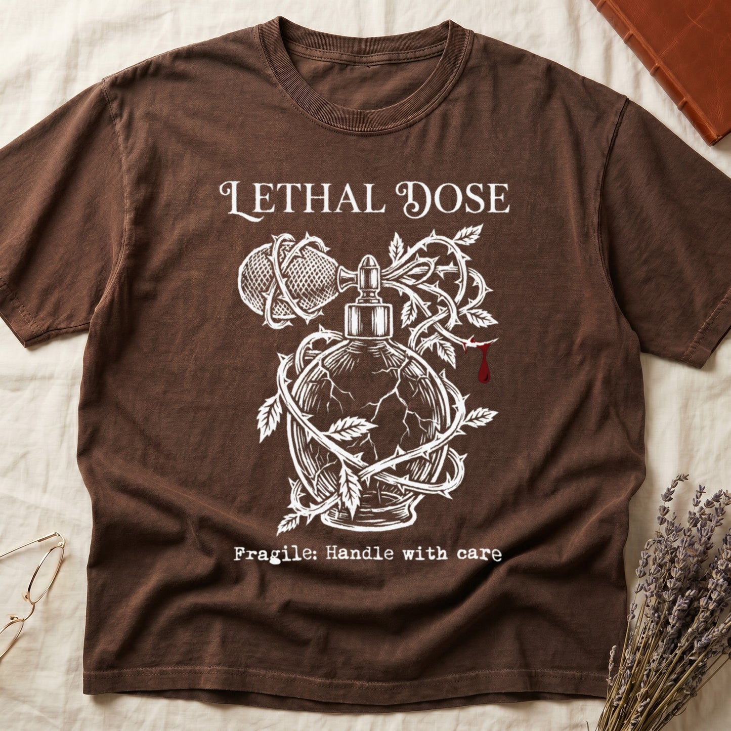Espresso tee with cracked perfume bottle wrapped in thorns, blood drop, "LETHAL DOSE" top, "Fragile: Handle with care" below.