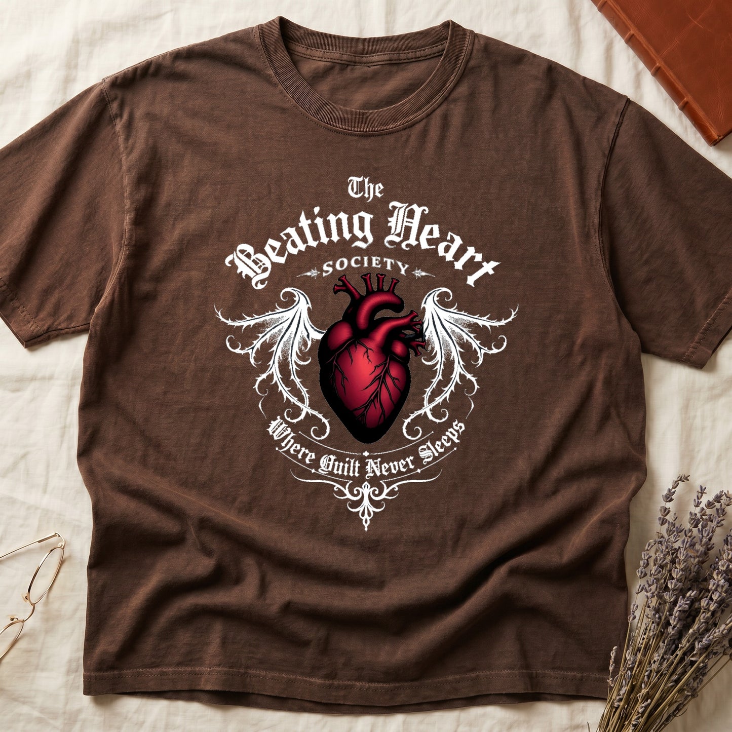 Espresso tee with anatomical red heart, gothic wings, "The Beating Heart SOCIETY," "Where Guilt Never Sleeps" below.