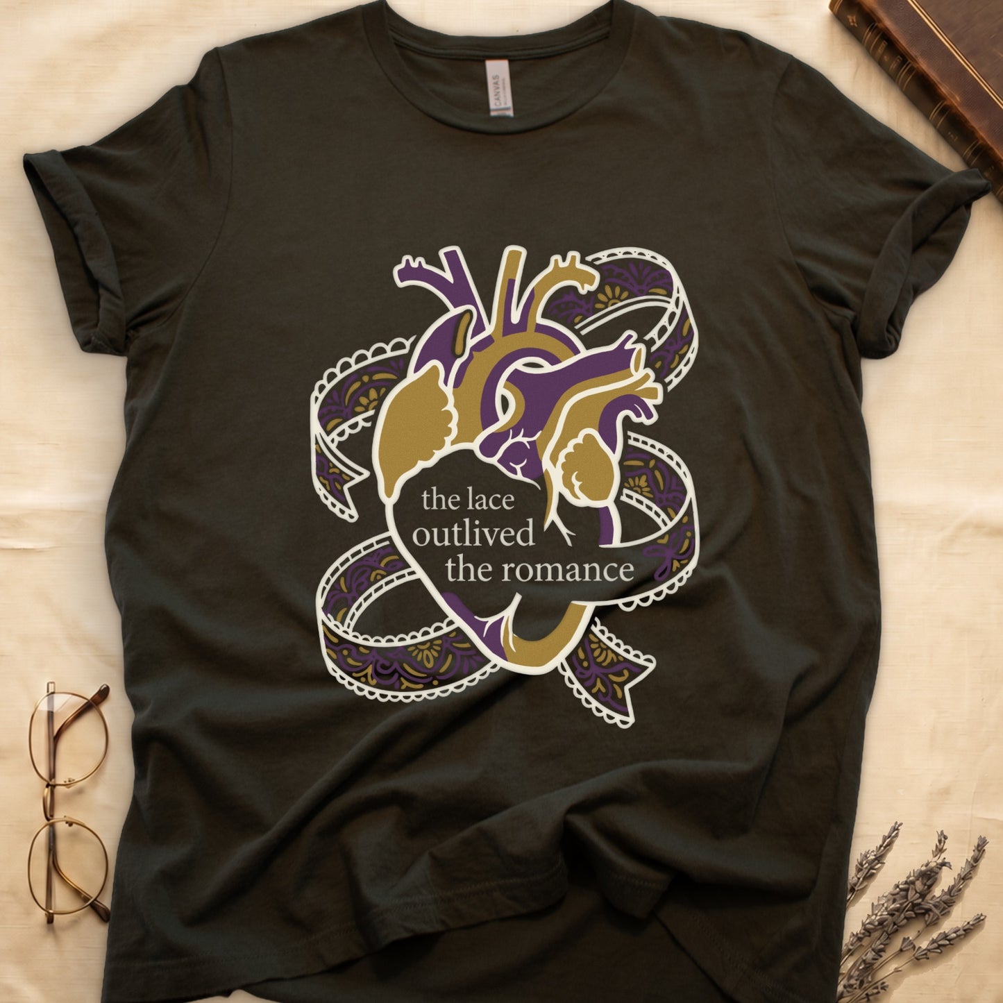 Military Green tee with anatomical heart in purple and gold wrapped in lace ribbons, "the lace outlived the romance" in serif.