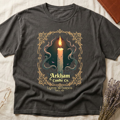 Pepper tee with lit candle, smoke, ornate gold filigree border, "Arkham Candle Co.," "Lighting the Darkness Since 1920."